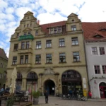 Ehemaliges Gasthaus “Zum Roten Hirsch”. Kopf und <a href="http://nightphotos.de/koken/content/meissen-hirschhaus-gasthaus-zum-roten-hirsch-wohn-und-geschaeftshaus-erbaut-1624-in-neurenaissance-renoviert-1901-markt-2-portal/"target="_blank" rel="noopener">Hirschhaus-Portal</a> (Ausschnitt) wurden dem ursprünglichen Gebäude entnommen und an den Neubau von 1901 angefügt