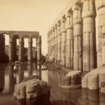 Der überflutete Hof von Amenhotep III. im Luxor-Tempel ca. 1860-1869 (<a href="https://en.wikipedia.org/wiki/Antonio_Beato"target="_blank" rel="noopener">Antonio Beato</a>) – <a href="https://www.meisterdrucke.com/kunstdrucke/Antonio-Beato/1589491/Der-%C3%BCberflutete-Hof-von-Amenhotep-III-im-Luxor-Tempel.html"target="_blank" rel="noopener">Quelle Foto</a>