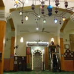 Der schön ausgeleuchtete Innenraum mit der Gebetsnische (<a href="https://de.wikipedia.org/wiki/Mihr%C4%81b"target="_blank" rel="noopener">Mihrāb</a>). Die Uhren rechts waren gut gemeint, schienen jedoch alle nicht zu funktionieren